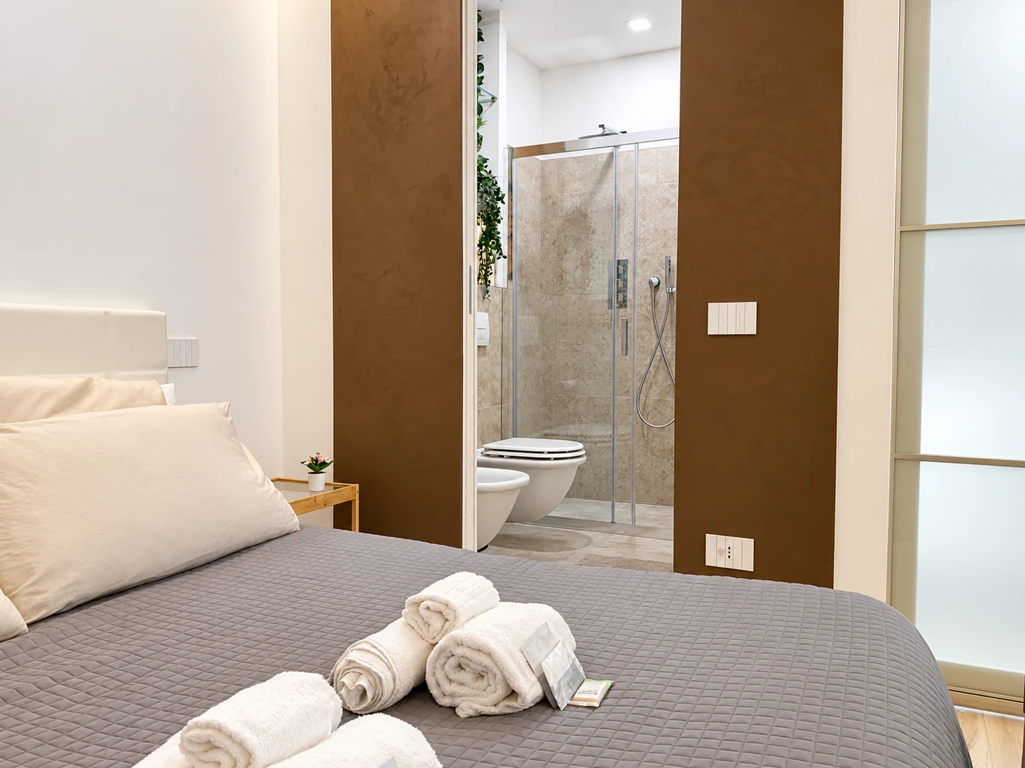Contemporary bedroom with en-suite bathroom, warm natural finishes and neatly arranged towels