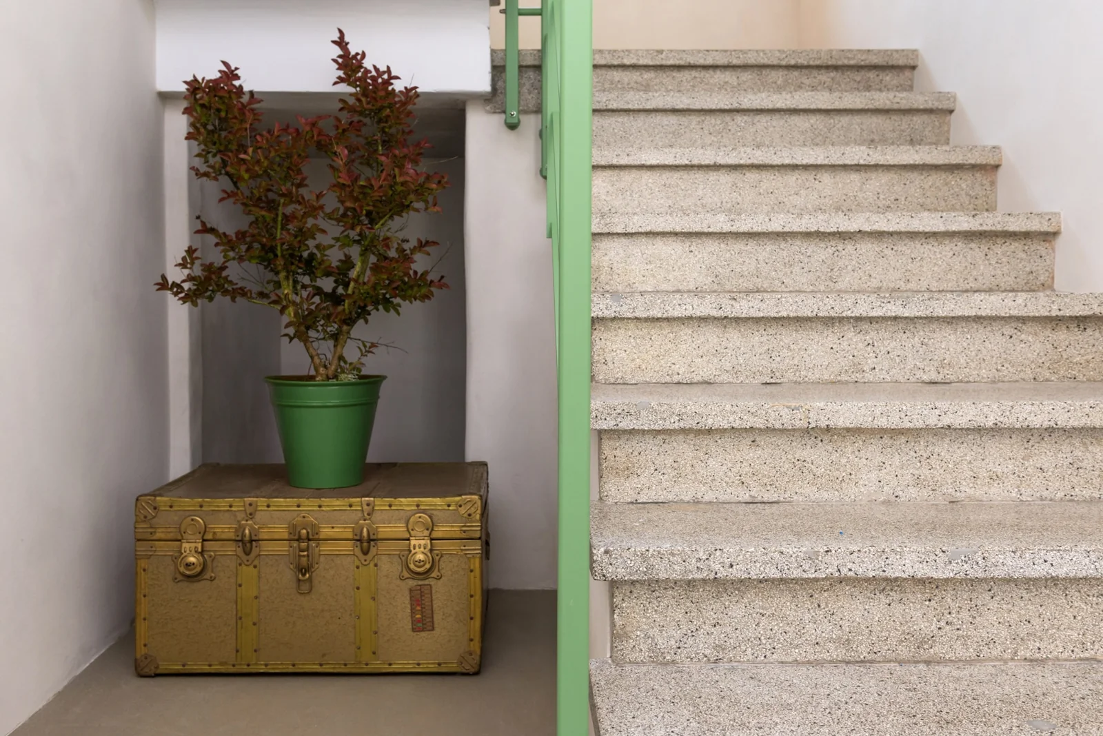 Terrazzo staircase with green railing and vintage trunk